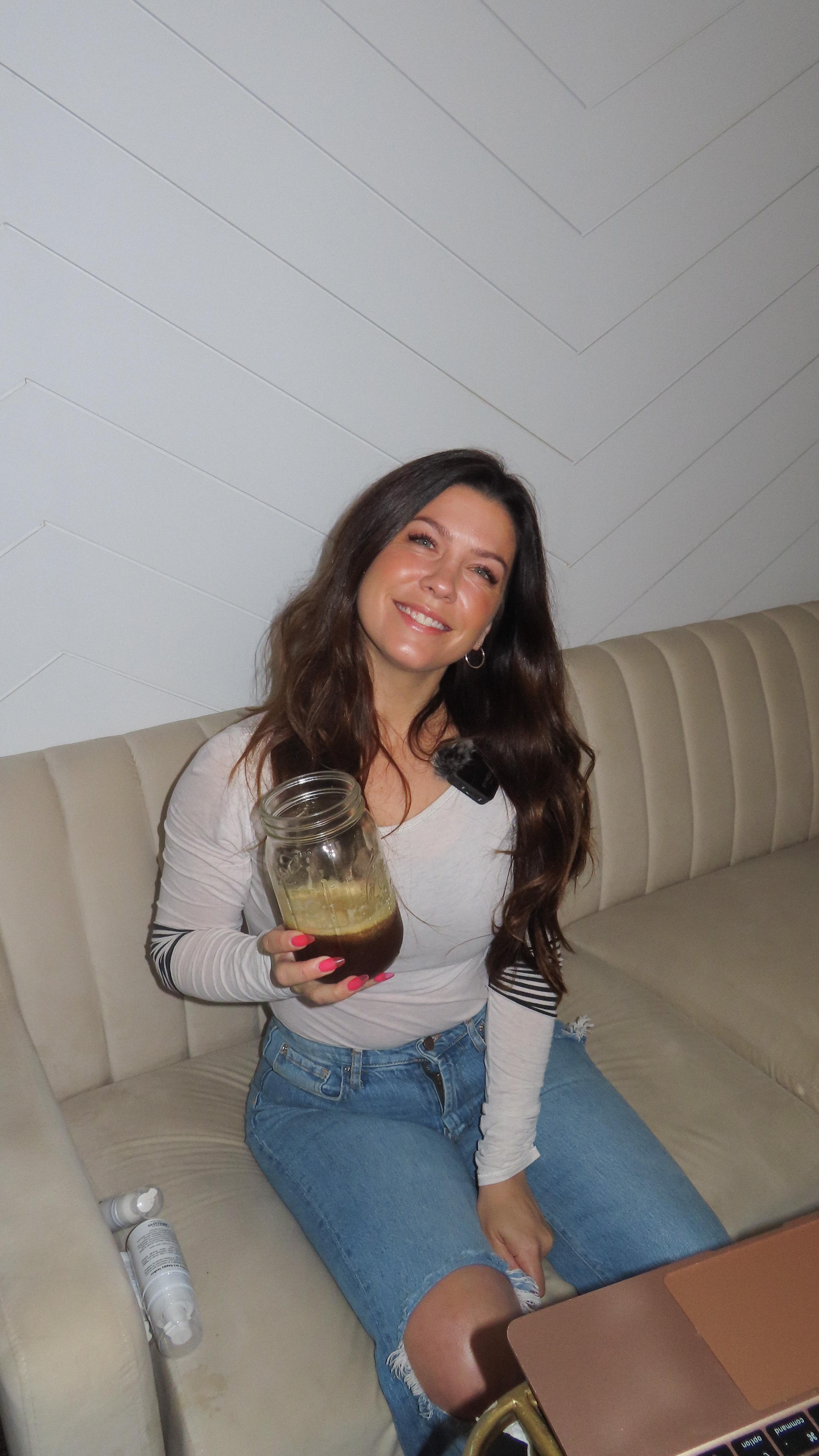 Danielle Rae laughing on a cream couch, holding a drink